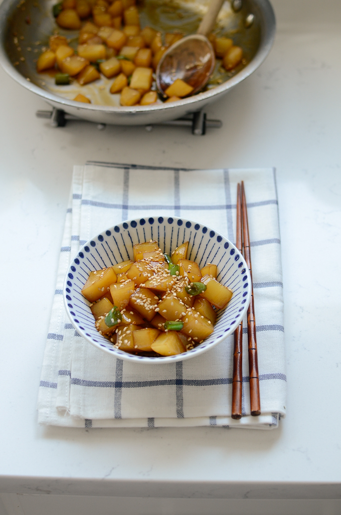 Korean potato side dish is garnished with sesame seeds and plated in a bowl.