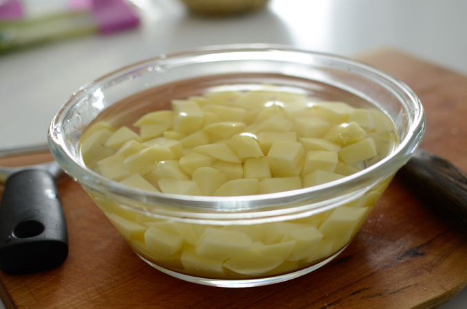 Cubed potato pieces are soaking in water in a bowl.