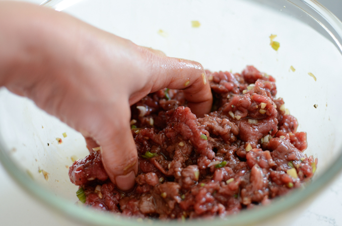 A hand is mixing up beef with marinade in a bowl.