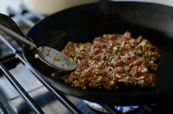 A spoonful of marinated bulgogi is spread thinly in a skillet on the stove.
