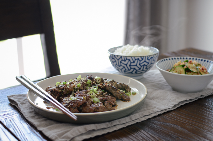 A plate of crispy beef is served with rice and cucumber side dish.