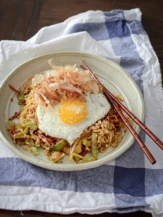 Quick ramen and vegetable stir-fry is topped with fried egg and bonito flakes in a bowl.
