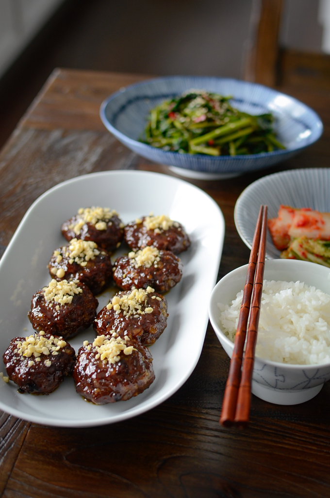 Honey glazed Korean beef patties are garnished with minced pine nuts are served with rice and kimchi on the side.