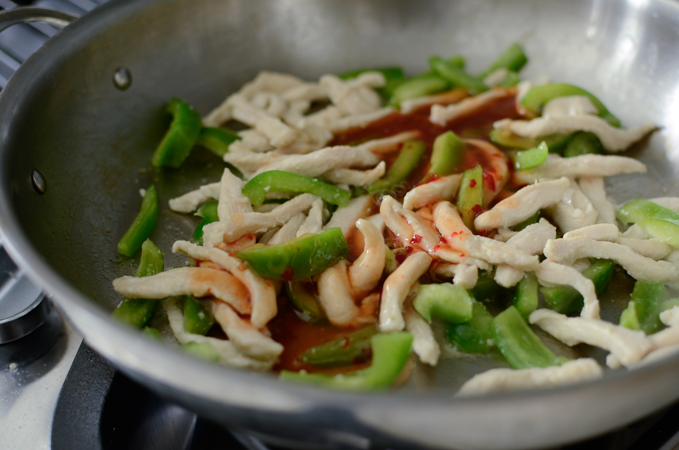 Stir-fried chicken breast and pepper strips in a skillet.