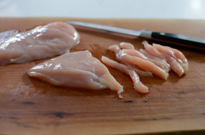 Chicken breast strips on a cutting board.