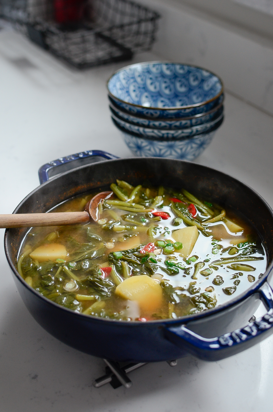 Turnip green and potato are made to a soup in a blue pot.