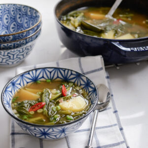 A Korean style turnip green potato soup is served in a blue bowl.