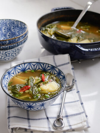 A Korean style turnip green potato soup is served in a blue bowl.