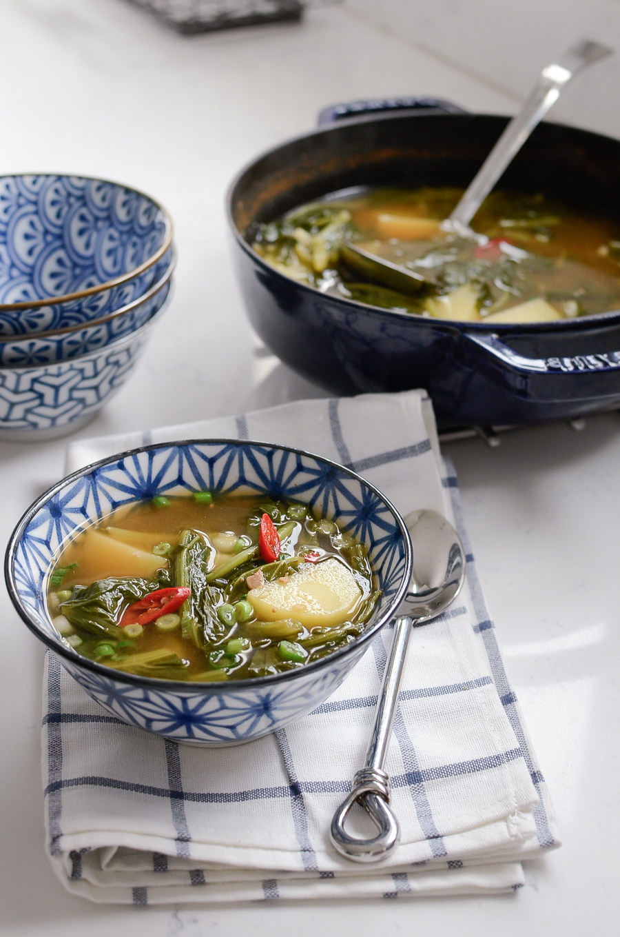 A Korean style turnip green potato soup is served in a blue bowl.