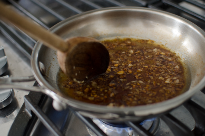 Soy sauce and sesame oil adds dark color to the garlic oil in a skillet.