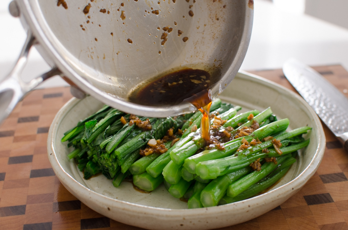 Hot garlic soy sauce oil in a skillet is pouring over blanched choy sum.