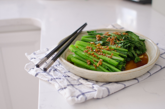 Blanched choy sum is dressed in soy garlic sauce in a serving plate with chopsticks.