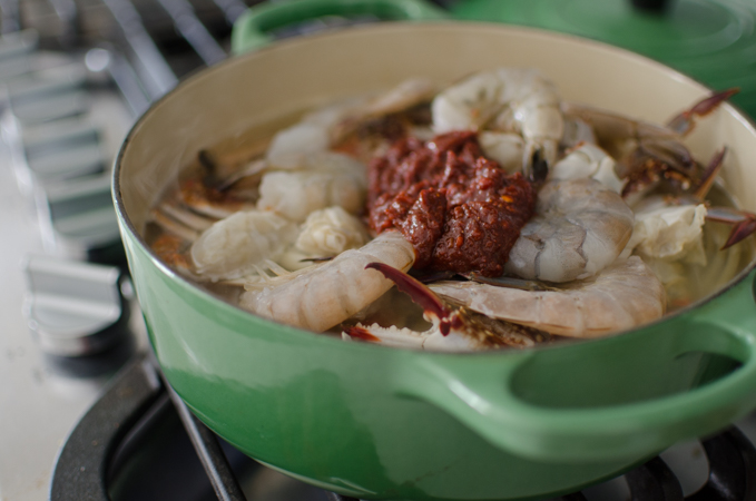 Crab pieces and shimps are in a pot with anchovy stock and seasoning paste is added.