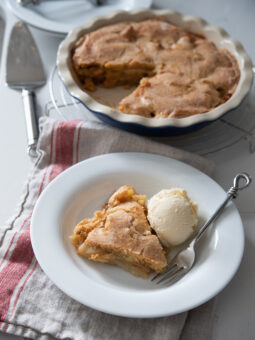 A piece of apple pie is cutout from pie dish and served with vanilla ice cream.