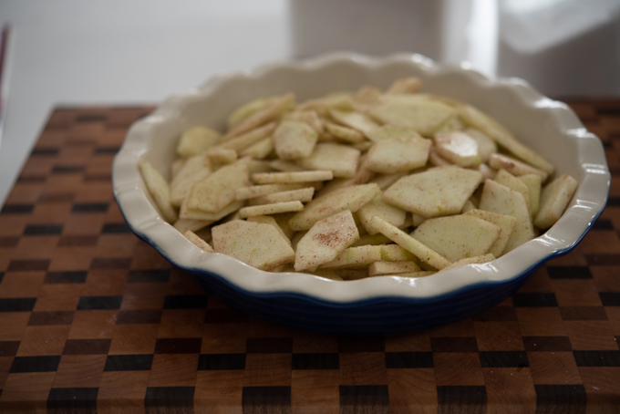 Cinnamon-spiced apple slices are filled in a pie dish.