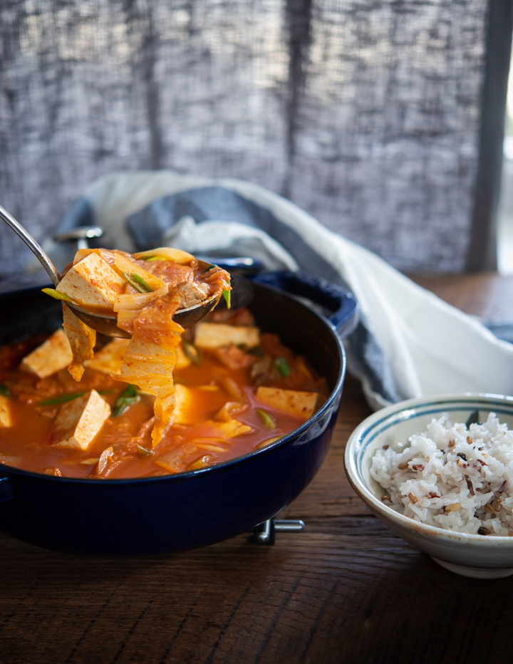 A ladle of kimchi tofu stew is served with a bowl of rice.