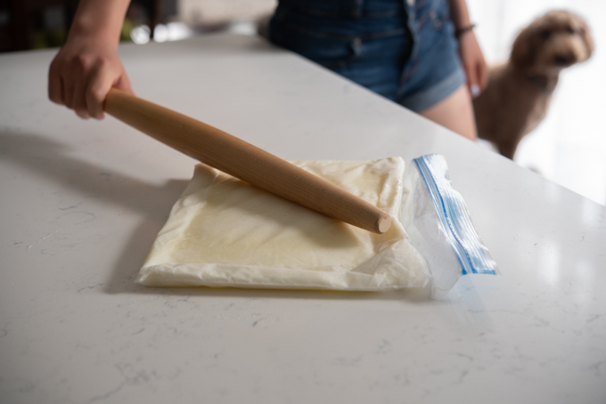 A wooden pin is smacking the frozen milk in a zip bag to loosen up.
