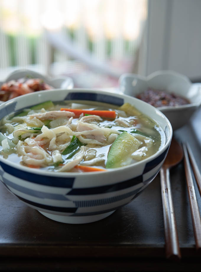 Korean knife cut chicken noodle soup (dak kalguksu) is served with soy chili sauce and kimchi.