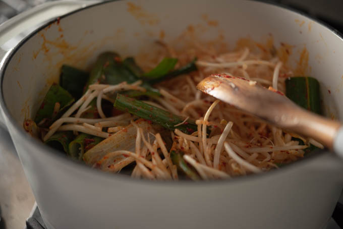 Leeks. chives, and bean sprouts are added to the chili oil in a pot.