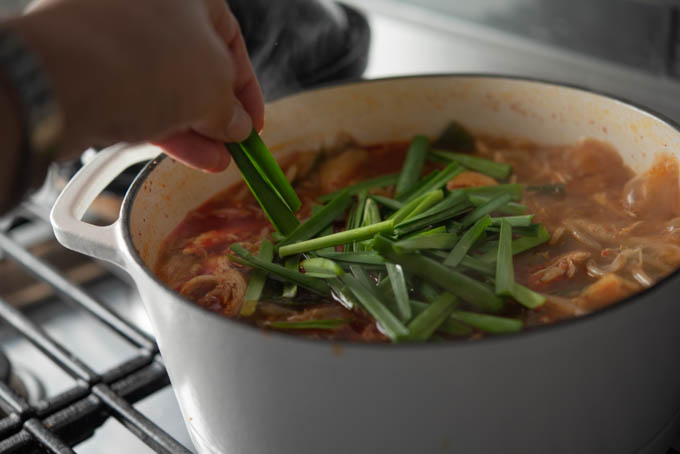 Asian chives are added to the simmering spicy chicken soup in a pot.