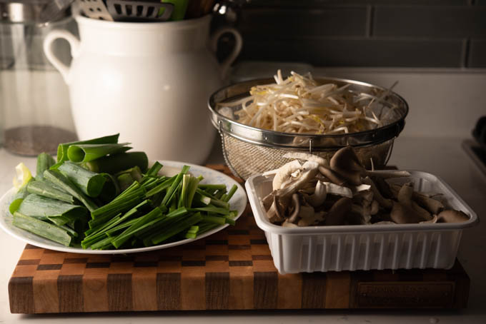 Asian chives, mushroom, and bean sprouts are placed on the wooden board.