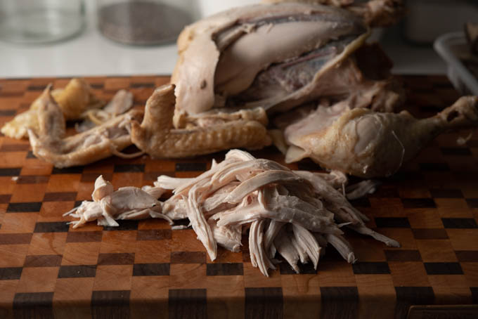 A boiled whole chicken is being shredded into bite size pieces.