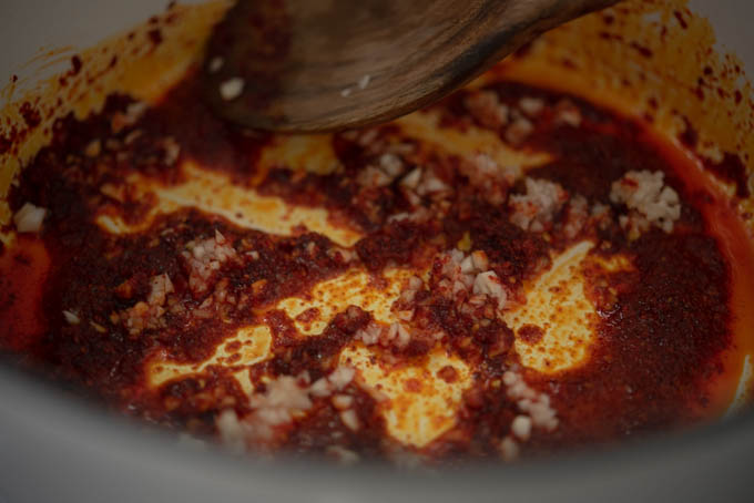 Minced garlic is cooking in a chili oil in a pot.