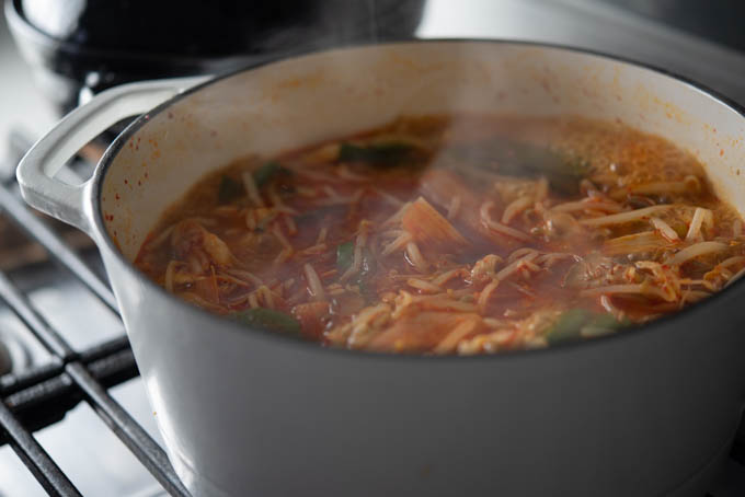 Various vegetables are simmering in a spicy broth in a pot over the stove.