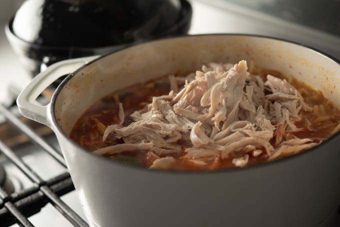 Shredded chicken is added to the spicy vegetabel in the broth.