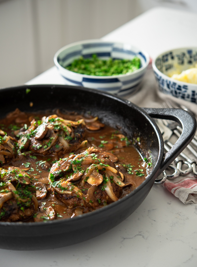 Salisbury Steak with Mushroom Onion Gravy is cooked in a cast iron skillet.