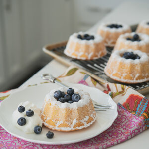 Hot milk mini bundt cakes are garnished with fresh blueberries and cream.