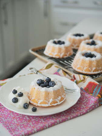 Hot milk mini bundt cakes are garnished with fresh blueberries and cream.
