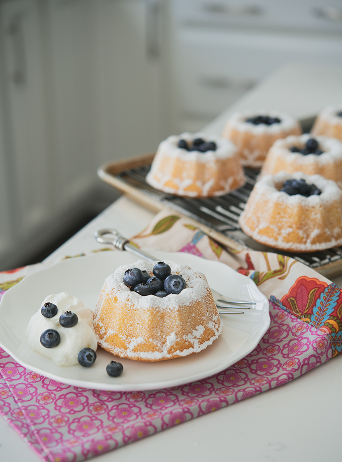 Hot milk mini bundt cakes are garnished with fresh blueberries and cream.