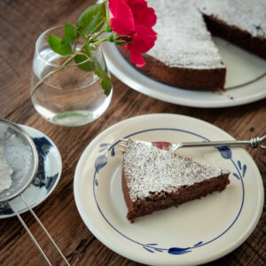 A slice of torta Caprese is garnished with powdered sugar and a rose.