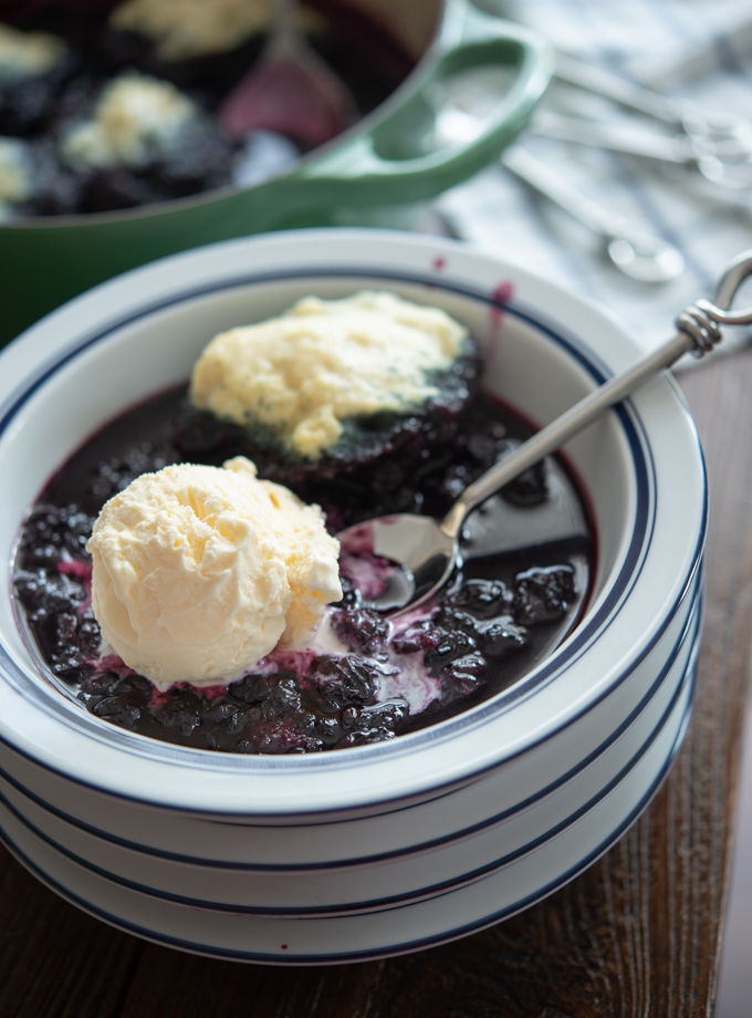 Blueberry dumplings are served with vanilla ice cream in a blue rimmed white serving bowl.