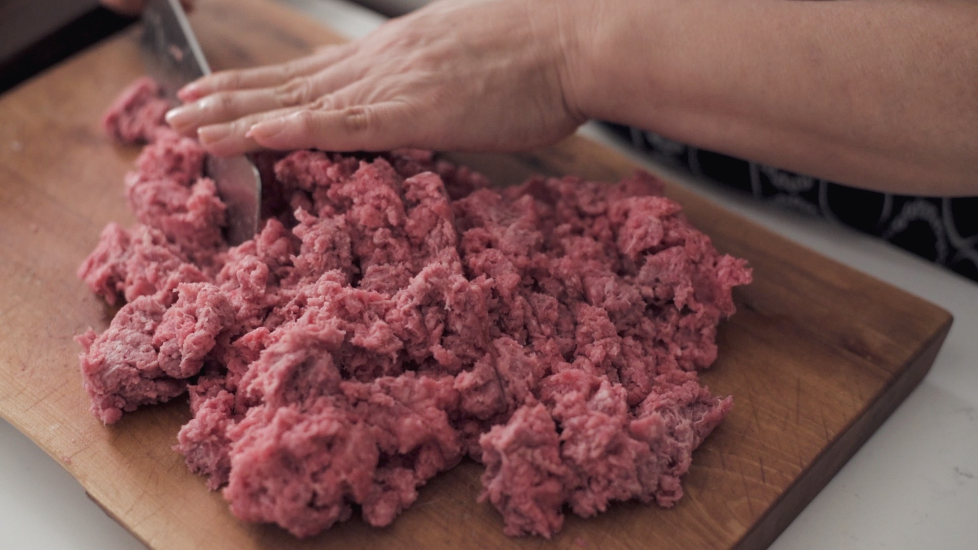A knife chopping ground beef brisket.