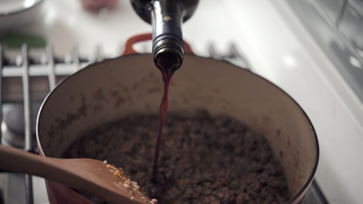 Red wine is added to the ragu sauce in a pot.