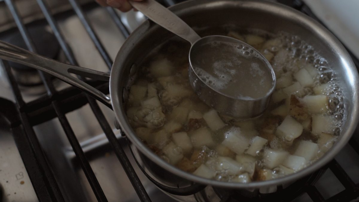 Chopped potatoes are boiling in a pot and a little bit of liquid is reserved.