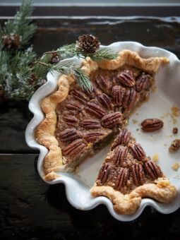 A slice of no corn syrup pecan pie in a white pie pan is ready to serve.