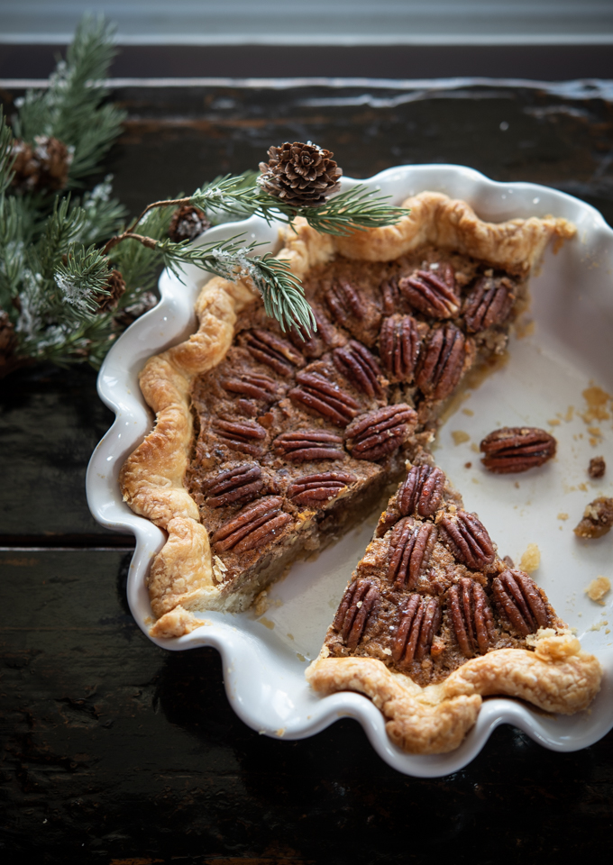 A slice of no corn syrup pecan pie in a white pie pan is ready to serve.