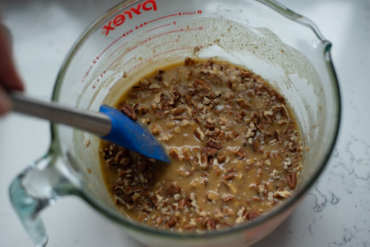 Pecan pie filling ingredients are mixed in a bow with a spatula.