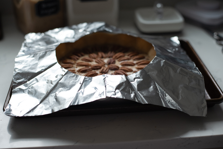 A piece of foil with a hole in the middle is covering the pecan pie.
