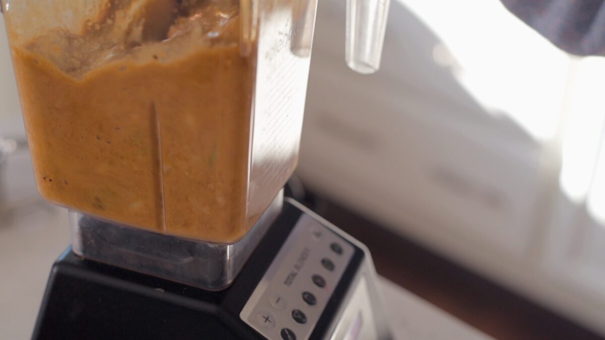A blender is pureeing onion, garlic and fruit mixture with soy sauce.