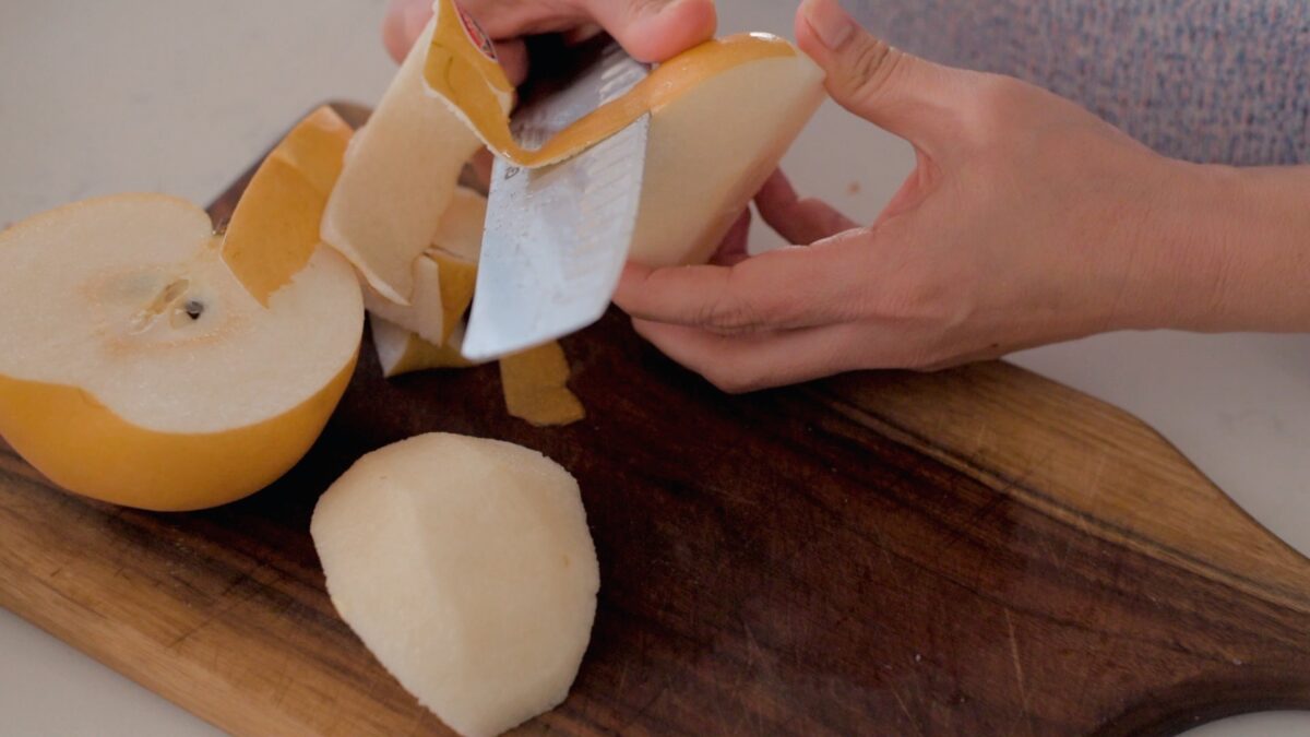 Korean pear cut in half and being peeled by a knife 