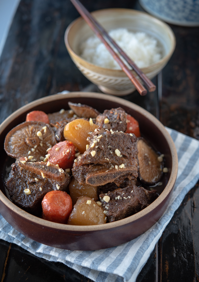 Braised Korean beef ribs with radish and carrot are served in a serving dish garnished with minced walnut