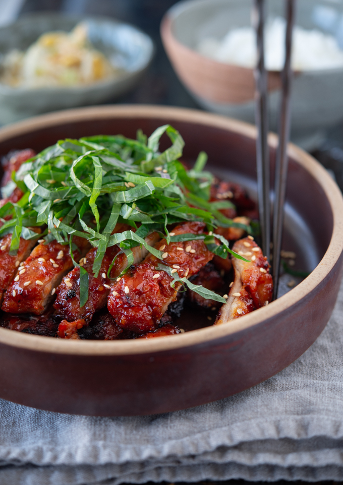 Korean BBQ chicken is garnished sliced perilla leaves and sesame seeds in a stone plate.