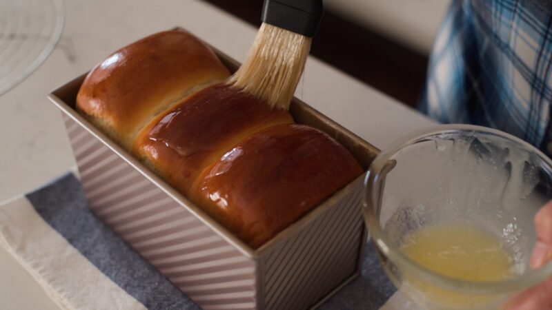 Brushing melted butter on milk bread.