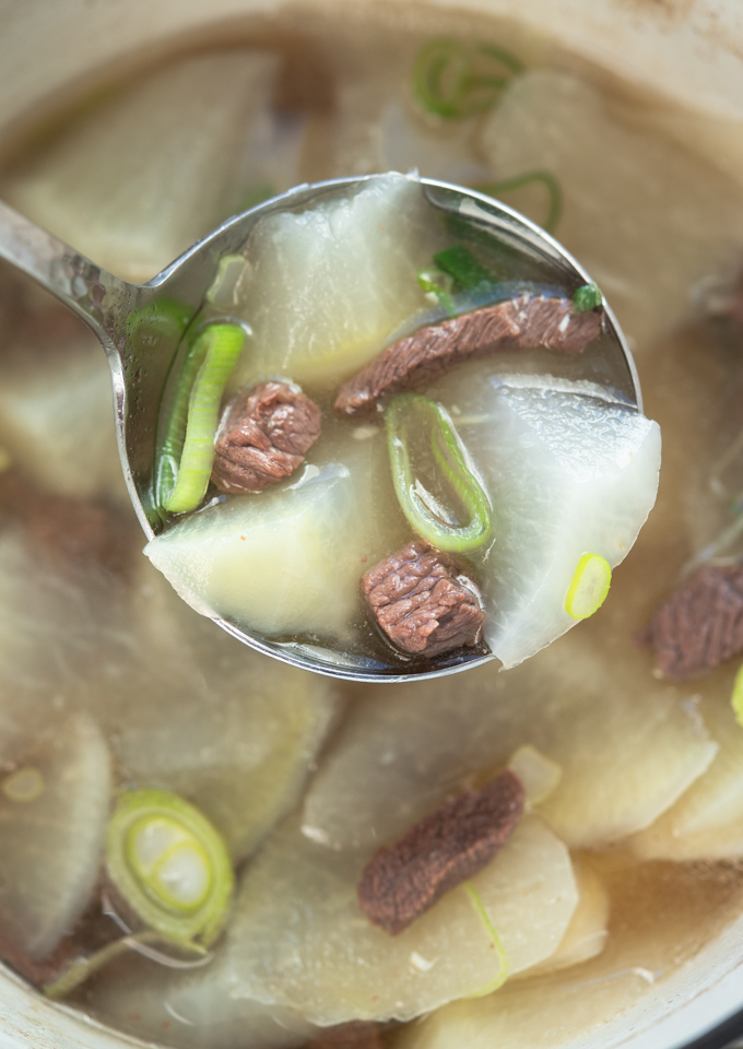 A ladle of beef and Korean radish soup has translucent broth.
