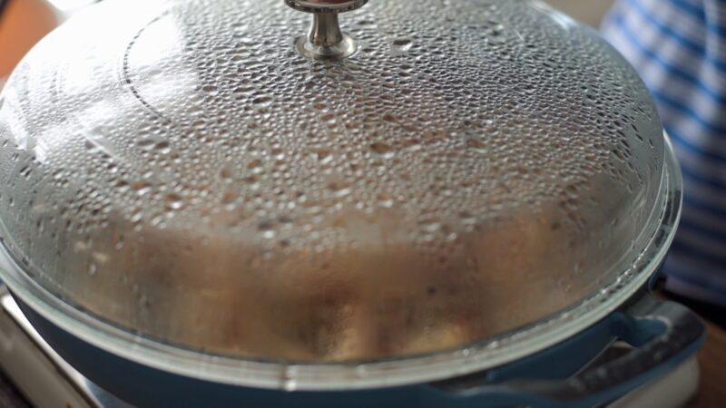 Browned chicken wings in a pan is covered with a lid.