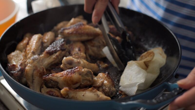 A piece of paper towel is wiping off extra fat in the pan.